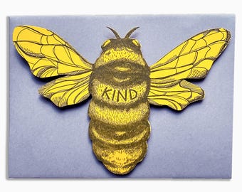 以下が含まれることがあります： 「KIND」の文字が書かれた、黄色と黒のハチのイラスト。薄紫色の背景に配置されています。ハチは詳細な羽を持っており、デザインの焦点となっており、優しさというテーマを示唆しています。