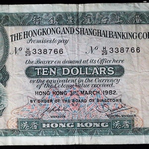 May include: A vintage ten dollar banknote from The Hongkong and Shanghai Banking Corporation, dated 31st March 1982. The paper currency features a green and white intricate guilloche pattern, a portrait of a woman, and a coat of arms on the left side.