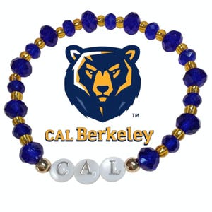 May include: A beaded bracelet featuring the Cal Berkeley logo and text. The bracelet has blue faceted beads and gold-colored spacer beads. The letters "C", "A", and "L" are spelled out in white beads. The Cal Berkeley logo is a gold bear head on a navy blue background.