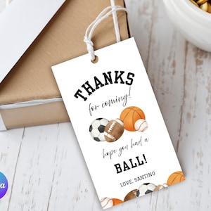 May include: A white gift tag with the text "Thanks for coming!" and "hope you had a BALL!" features illustrations of a soccer ball, football, basketball, and baseball. The tag is tied to a brown gift box with a white ribbon.