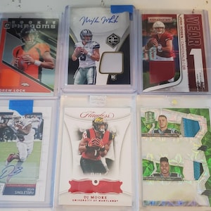Könnte beinhalten: Eine Sammlung von sechs Football-Sammelkarten in Schutzhüllen. Die Karten zeigen Bilder von Spielern, Teamlogos und Text, darunter "ROOKIE", "SCORE" und Spielernamen wie Drew Lock und DJ Moore. Die Karten sind in verschiedenen Farben.