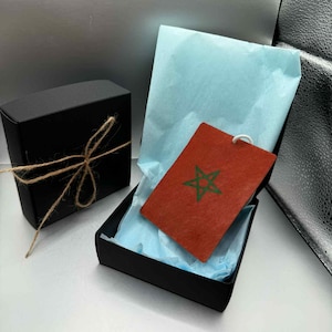 May include: Two black gift boxes, one tied with twine, the other open to reveal a red tag with a green star and tissue paper. The tag has a white string attached. The open box is lined with light blue tissue paper.