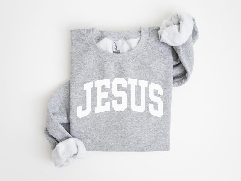 Puede incluir: Sudadera gris jaspeado con la palabra "JESUS" impresa en letras blancas grandes en la parte delantera. Las mangas est&aacute;n dobladas, revelando el interior blanco. Prenda casual y c&oacute;moda.