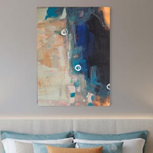 May include: An abstract painting with a mix of colors, including blue, orange, and white, hangs above a bed. The bed has a teal comforter, pillows, and a gray throw blanket. Two blue lamps sit on wooden nightstands.