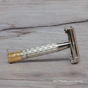 May include: A silver and gold safety razor with a textured handle and a gold-colored end. The razor head is silver and rectangular. The text "Back Roads Gold Plating" is visible in the image.