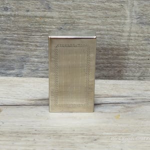 May include: A rectangular silver-colored metal box with a decorative, textured border and vertical lines. The box is standing upright on a wooden surface. The text "Back Roads Gold Replating" is visible at the bottom right.