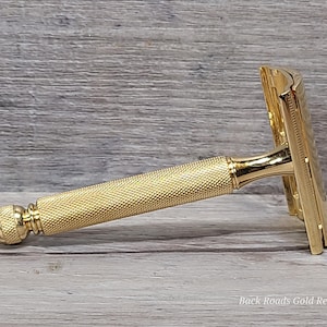 May include: A gold-colored safety razor with a textured handle and a classic design. The razor is made of metal and has a shiny finish. The razor is designed for shaving and grooming.