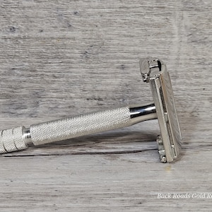 May include: A silver safety razor with a textured handle. The razor head is rectangular and the handle is cylindrical with a diamond pattern. The text "Back Roads Gold Replating" is visible at the bottom.