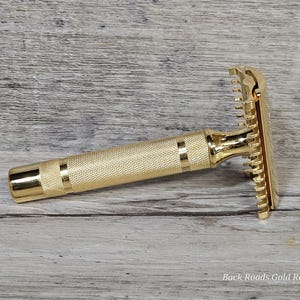 May include: A gold-colored safety razor with a textured handle and a comb-like head. The razor is made of metal and has a shiny finish. The text "Back Roads Gold Replating" is visible at the bottom of the image.