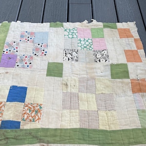 May include: A patchwork quilt with a white background and various colored squares. The squares are made of different fabrics and patterns, including floral, geometric, and solid colors. The quilt is edged with a green border.