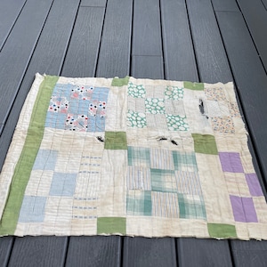 May include: A vintage patchwork quilt with a white background and green, blue, and purple squares. The quilt has a worn and faded appearance, with some holes and tears.