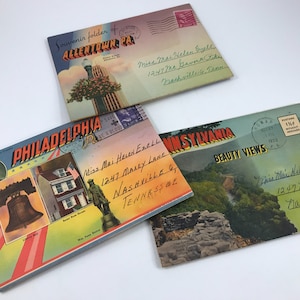 Może przedstawiać: Trzy vintage'owe foldery z pocztówkami pamiątkowymi z kolorowymi ilustracjami i ręcznie napisanymi adresami. Foldery przedstawiają zdjęcia Allentown w Pensylwanii, Filadelfii w Pensylwanii i Pięknych Widoków Pensylwanii.
