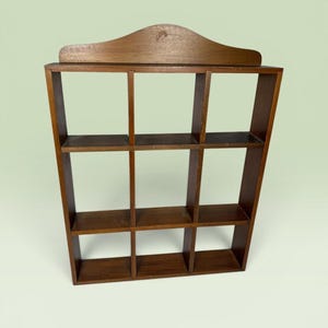 May include: A vintage, dark brown wooden shelf with nine cubby holes. The shelf has a curved top and a slightly angled design, creating a unique display piece. The wood grain is visible, adding to its rustic charm. Ideal for displaying small collectibles or decorative items.