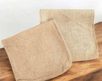 May include: Two brown burlap fabric bags, one folded on top of the other, on a wooden surface.
