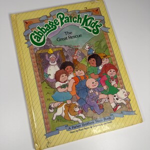 Puede incluir: Un libro de cuentos vintage de Cabbage Patch Kids titulado "The Great Rescue". La portada presenta un fondo amarillo con ilustraciones de los personajes de Cabbage Patch Kids, un cerdo y un perro. El libro es un libro de cuentos de Parker Brothers.