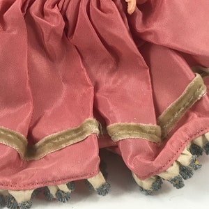 May include: A pink satin doll dress with a brown velvet trim and a white lace ruffle with blue beading.