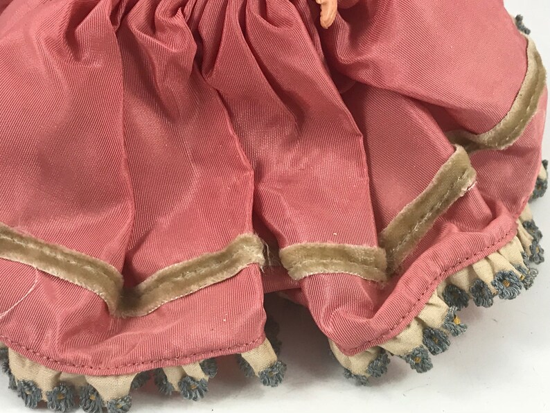 May include: A pink satin doll dress with a brown velvet trim and a white lace ruffle with blue beading.