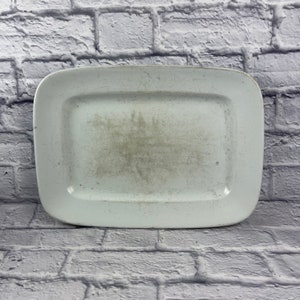 May include: A white rectangular serving platter with a slightly raised rim. The platter has a worn, vintage look with visible scratches and marks.