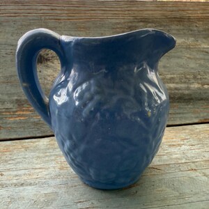 May include: A blue ceramic pitcher with a textured, embossed design. The pitcher has a wide mouth and a handle.