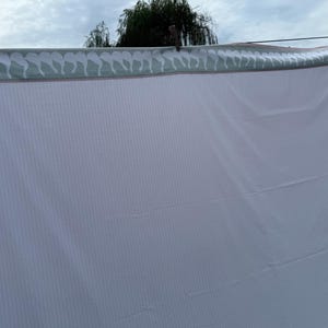 May include: A white sheet with vertical stripes hangs from a washing line. The top edge has a decorative border with a repeating pattern of white seahorses on a light green background. A wooden clothes peg secures the sheet.