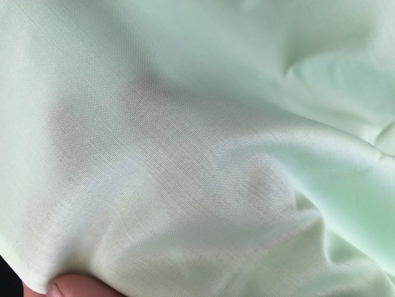 K&ouml;nnte beinhalten: Nahaufnahme eines hellgr&uuml;nen Stoffes mit glatter, seidenartiger Textur.