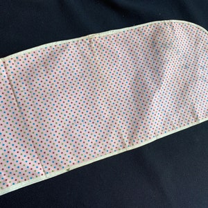 May include: A pink fabric with a white border and a polka dot pattern in red, blue, and green. The fabric is curved at one end.