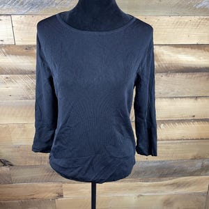 May include: A black, long-sleeved top with a boat neck. The top is made of a ribbed knit fabric and has three-quarter length sleeves. The garment is displayed on a black mannequin.