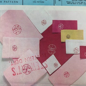 May include: A set of pink, white and red fabric squares with a red swirl design printed on each. The fabric squares are arranged on a white surface. The text "McCall's Blue Transfer" is printed at the top of the image.