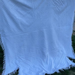 May include: White cotton blanket with a fringed edge. The blanket has a subtle embossed pattern.