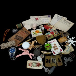 May include: A collection of vintage ephemera and small objects, including a doll head, dice, a heart-shaped box, buttons, keys, and a watch. Various colors and textures are visible, with a black background.