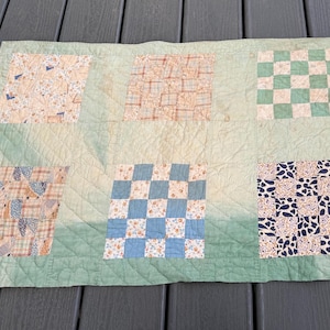 Può includere: Una trapunta vintage con sfondo verde chiaro e sei toppe quadrate. Le toppe presentano vari motivi, tra cui disegni a scacchi in blu e verde, e stampe floreali e a quadri in beige e marrone. La trapunta ha una trama trapuntata.