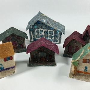Puede incluir: Una colección de casas en miniatura con tejados brillantes en varios colores, incluyendo azul, verde y burdeos. Las casas tienen diseños detallados de ventanas y puertas, creando una escena de pueblo encantadora y caprichosa. Ideal para la decoración navideña.