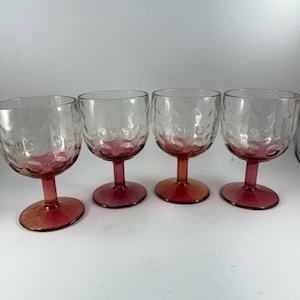 May include: Four clear wine glasses with textured bowls and red stems and bases. The glasses have a bubble-like pattern on the bowl. The stems and bases transition from red to a golden hue.