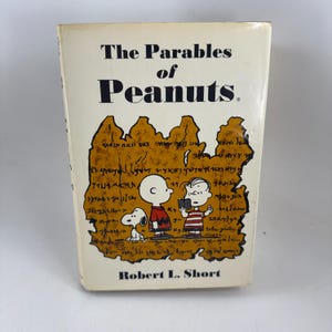 May include: A vintage book titled "The Parables of Peanuts" by Robert L. Short. The cover features a cream background with the title in black and a brown illustration of the Peanuts characters, including Snoopy, Charlie Brown, and Linus.