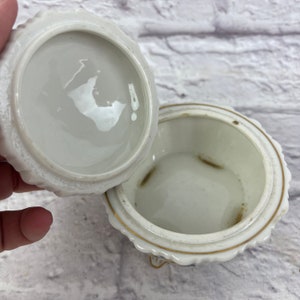 May include: White porcelain trinket box with a gold trim and floral design. The lid is open and the inside of the box is visible.
