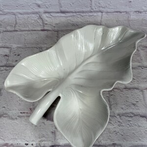 Puede incluir: Plato de servir de cerámica blanca con forma de hoja. El plato tiene forma de hoja grande con una vena prominente que recorre el centro. El plato es perfecto para servir aperitivos, entrantes o postres.