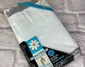 May include: A package of white, no-iron muslin pillowcases with a white daisy on a black background. The package says "Penn-Prest" and "Fashion Manor" with the text "Never Needs Ironing!" and "50% Polyester 50% Cotton No-Iron Muslin". The package also says "2 pillow cases 42 x 36 size before hemming".