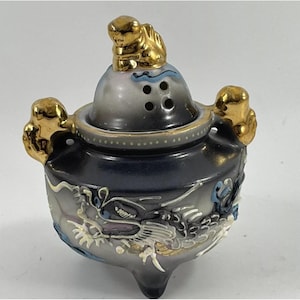 Op de afbeelding: Een keramische wierookbrander met een donkerblauwe en grijze afwerking, met een goudkleurige draak en accenten. Het deksel heeft een goudkleurige dierfiguur en luchtopeningen. De brander heeft drie kleine voetjes en goudkleurige handvatten.