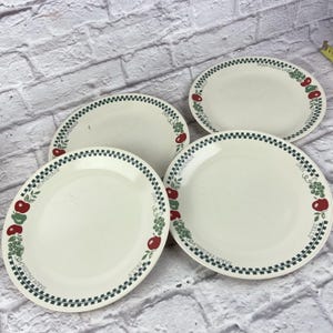 Könnte beinhalten: Vier cremefarbene ovale Teller mit einem grün-schwarzen Karomuster. Die Teller zeigen ein Design aus roten Äpfeln und grünen Trauben. Die Worte "Farm Fresh Jelly Homemade" sind am Rand der Teller aufgedruckt.
