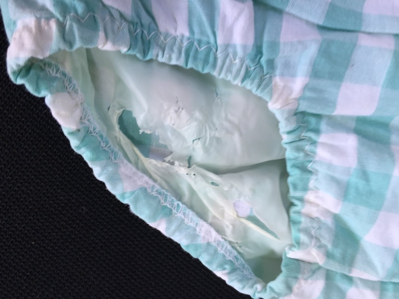 May include: A close-up of a green and white gingham fabric with a hole in the fabric. The fabric is gathered at the top and has a white seam.