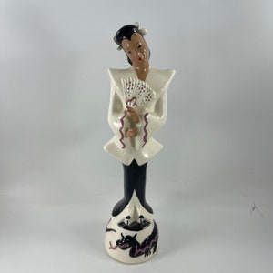 Può includere: Una statuetta in ceramica bianca di una donna con un abito bianco e nero che tiene un ventaglio. La donna è in piedi su una base con un disegno di drago bianco e nero.