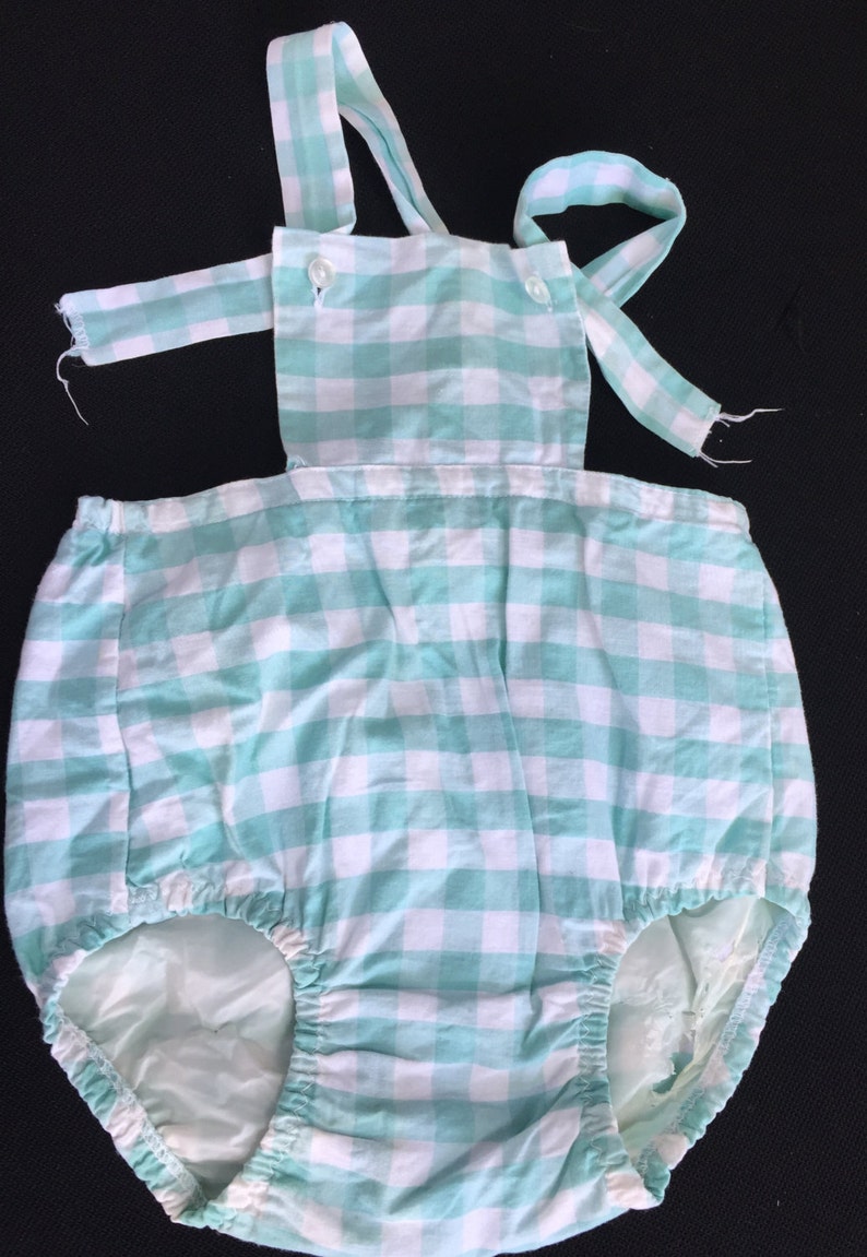May include: A light blue and white gingham baby onesie with straps. The onesie has a ruffled bottom and is made of a soft, comfortable fabric.