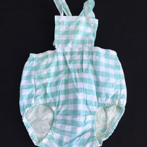 May include: A baby onesie with a green and white gingham pattern and straps. The onesie has a ruffled bottom and is made of a soft, comfortable fabric.