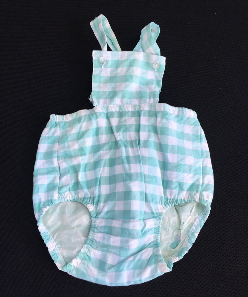 May include: A baby onesie with a green and white gingham pattern and straps. The onesie has a ruffled bottom and is made of a soft, comfortable fabric.