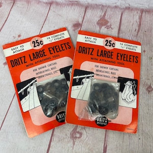 May include: Two packages of Dritz Large Eyelets with attaching tool. Each package contains 14 complete 1/4 inch eyelets and costs 25 cents. The packages are orange and white with black text. The eyelets are black and are packaged in clear plastic bags. The packages are for shower curtains, interlacings, bags, drawstrings, etc.