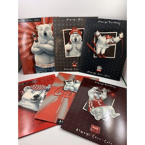 May include: A collection of Coca-Cola themed notebooks featuring the iconic polar bear mascot. Each notebook has a different design, with the bear in various poses, holding a bottle, playing baseball, and skiing. The notebooks have the Coca-Cola logo.