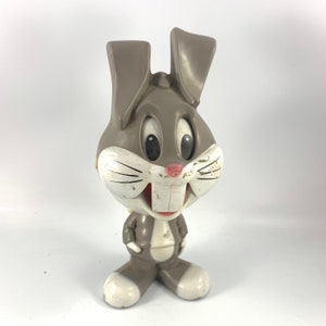 May include: A gray plastic toy rabbit with white accents. The rabbit has a wide smile and large, round eyes. The toy is slightly dirty and shows signs of wear.