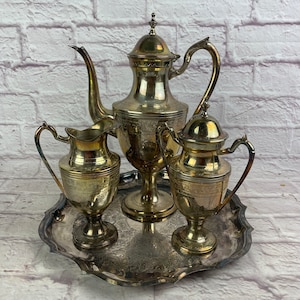 May include: A silver tea set with a teapot, creamer, and sugar bowl on a silver tray. The set has an ornate design and is in excellent condition.