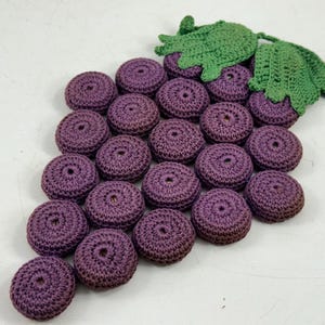 May include: A handmade crochet grape cluster with purple 'grapes' and green leaves. The round grapes are tightly crocheted, and the leaves have a detailed, textured appearance. This decorative item is likely used for home decor.