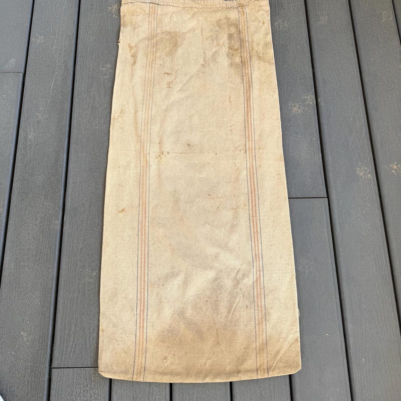 May include: A large, off-white canvas sack with red and blue stripes. The sack is made of a coarse, woven fabric and has a worn, vintage look.